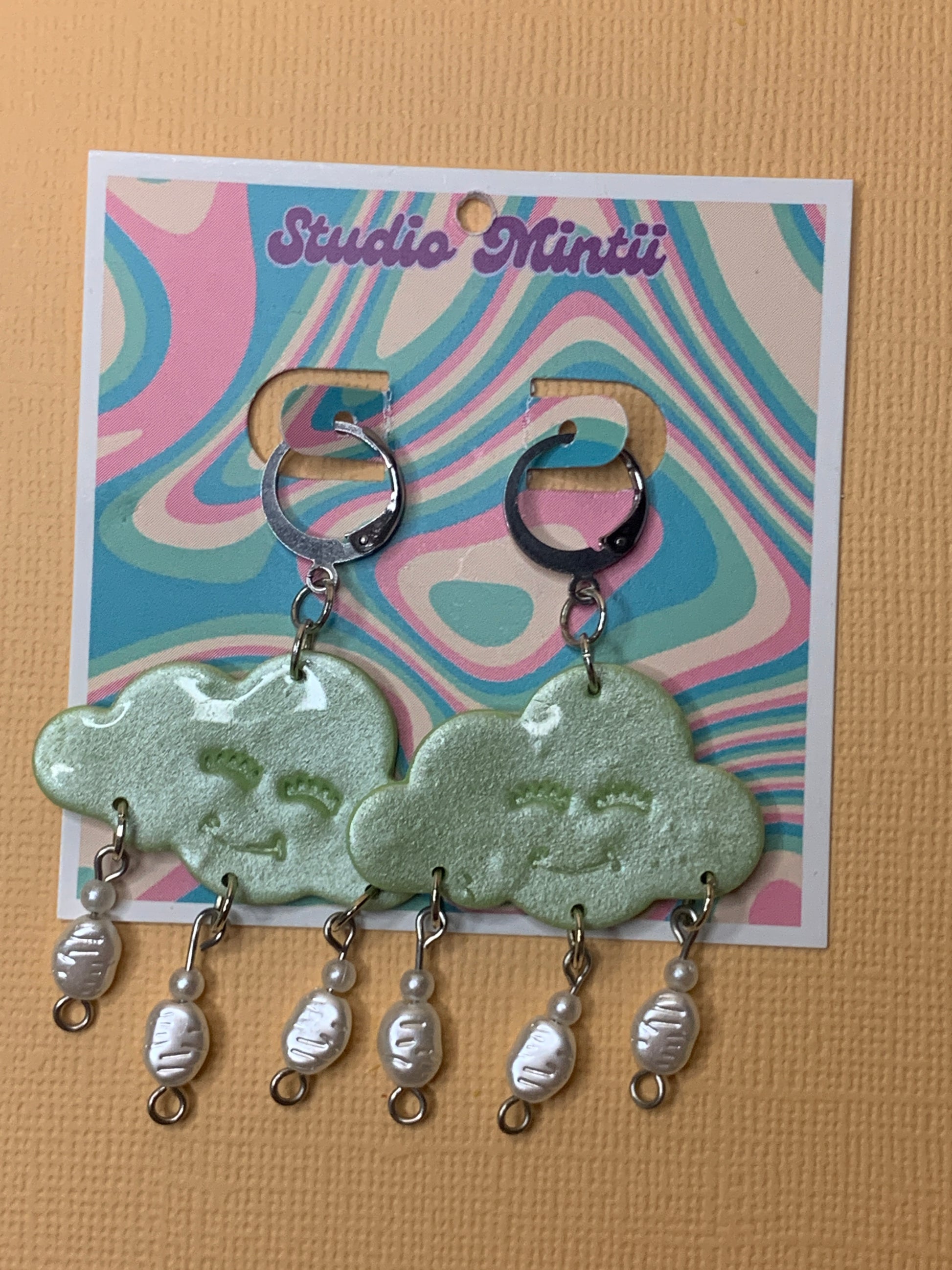 Green Happy Cloud Dangles - Studio Mintii Add some playful charm to your outfit with our Green Happy Cloud Dangles. These glittery green earrings are accented with faux pearls for a touch of elegance. Get ready to shine like a cloud on a sunny day! Note: Last image is an example of different types of bead detailing I can do. Options go from left to right as; Beads 1, 2, or 3  #